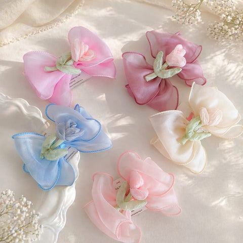 Set of five pastel-colored floral buds in bow hair clips on a soft fabric background