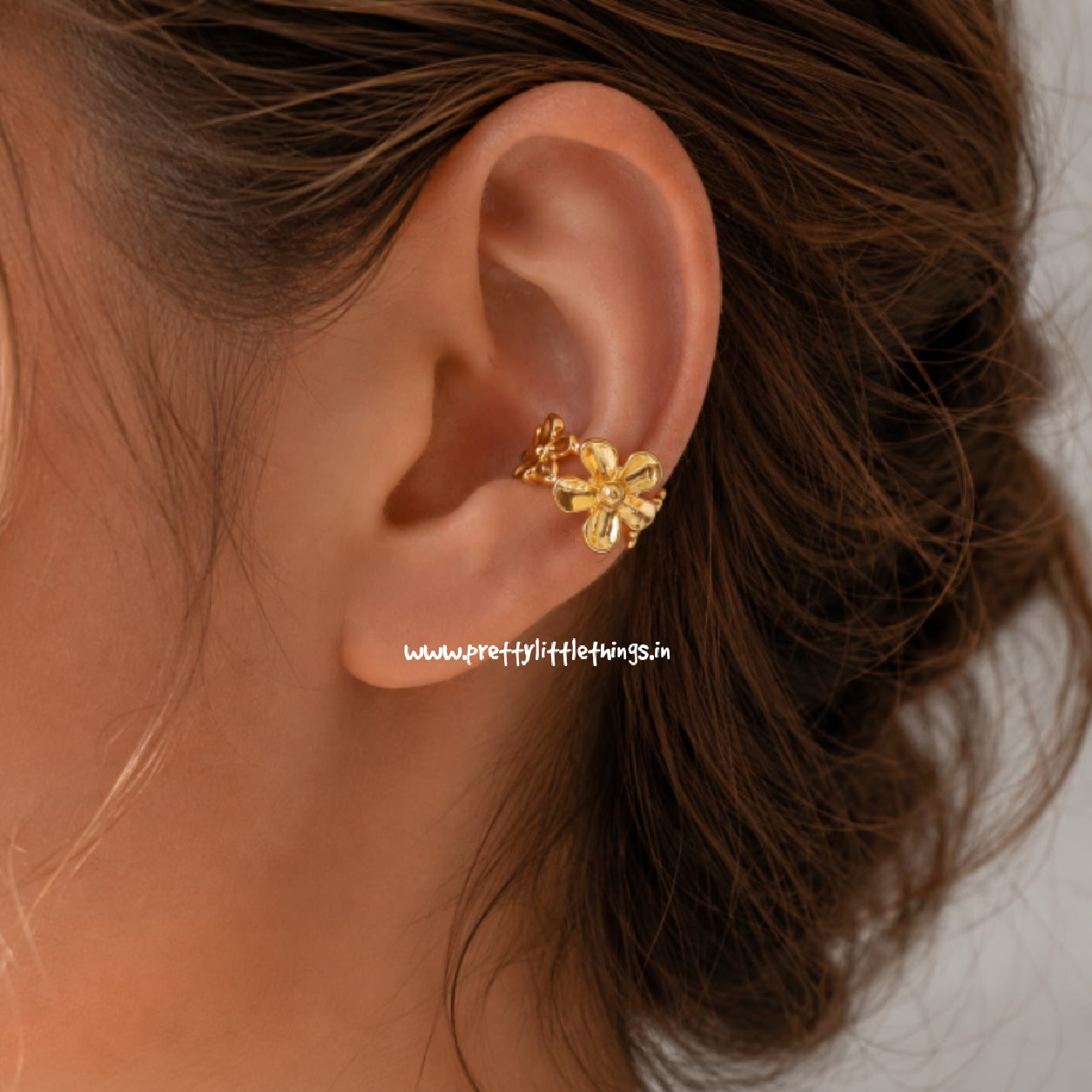 Gold flower shaped earcuff worn on an ear with brown hair.