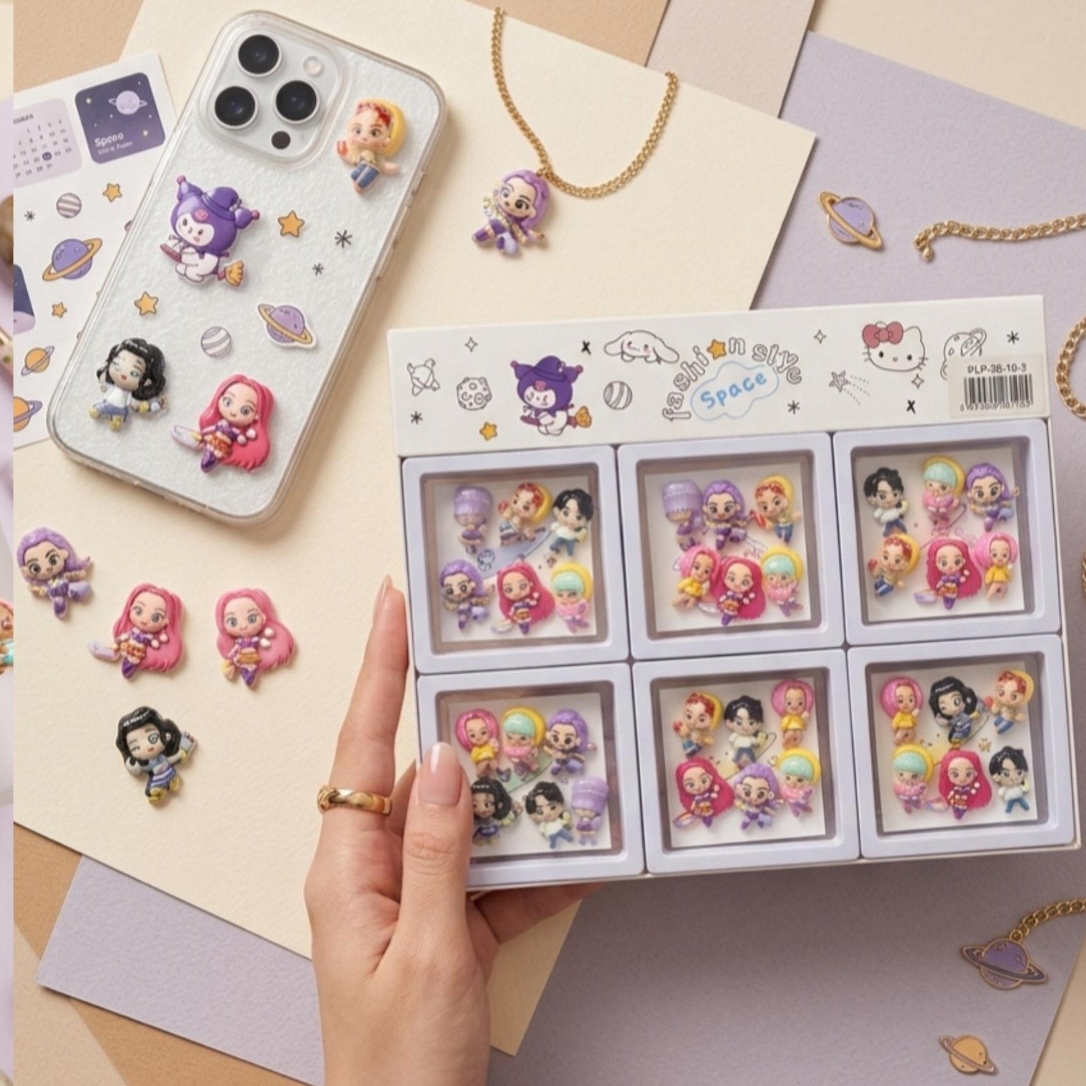Hand holding a box of small figurines  with some stitcking to a phone case and packs of stickers featuring similar designs on a neutral background.