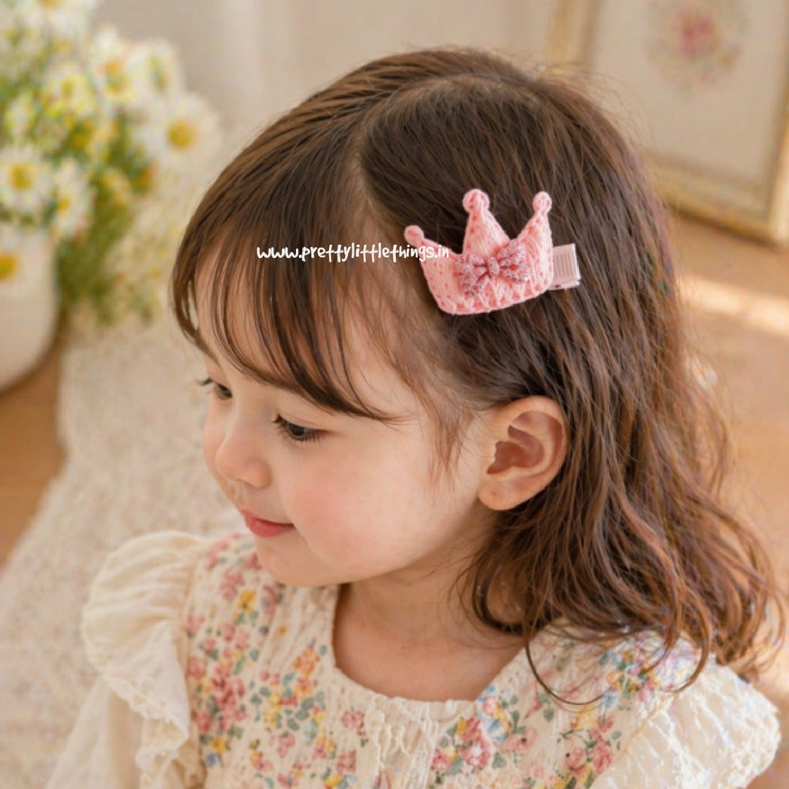 Child wearing a floral blouse and pink crown hair accessory with a soft, blurred background.