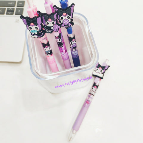 Set of cartoon cat-themed pens in a clear container on a white surface with a laptop.