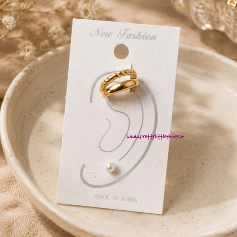 Golden double band earcuff with stud earring on a white card with placed on a beige plate.