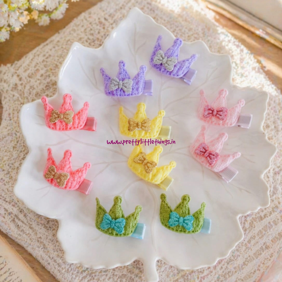 Colorful crown-shaped hair accessories on a white dish with flowers and a book in the background.